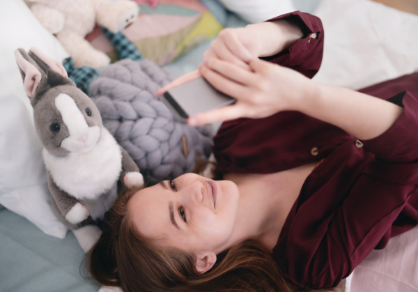 Top view of happy young girl smiling and taking selfie with smartphone on bed, online dating concept.