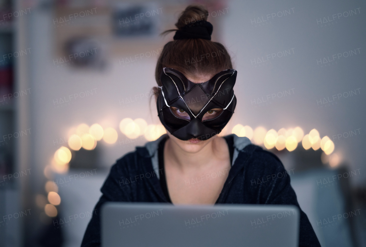 Front view of young girl with cat mask and laptop sitting, online dating and abuse concept.