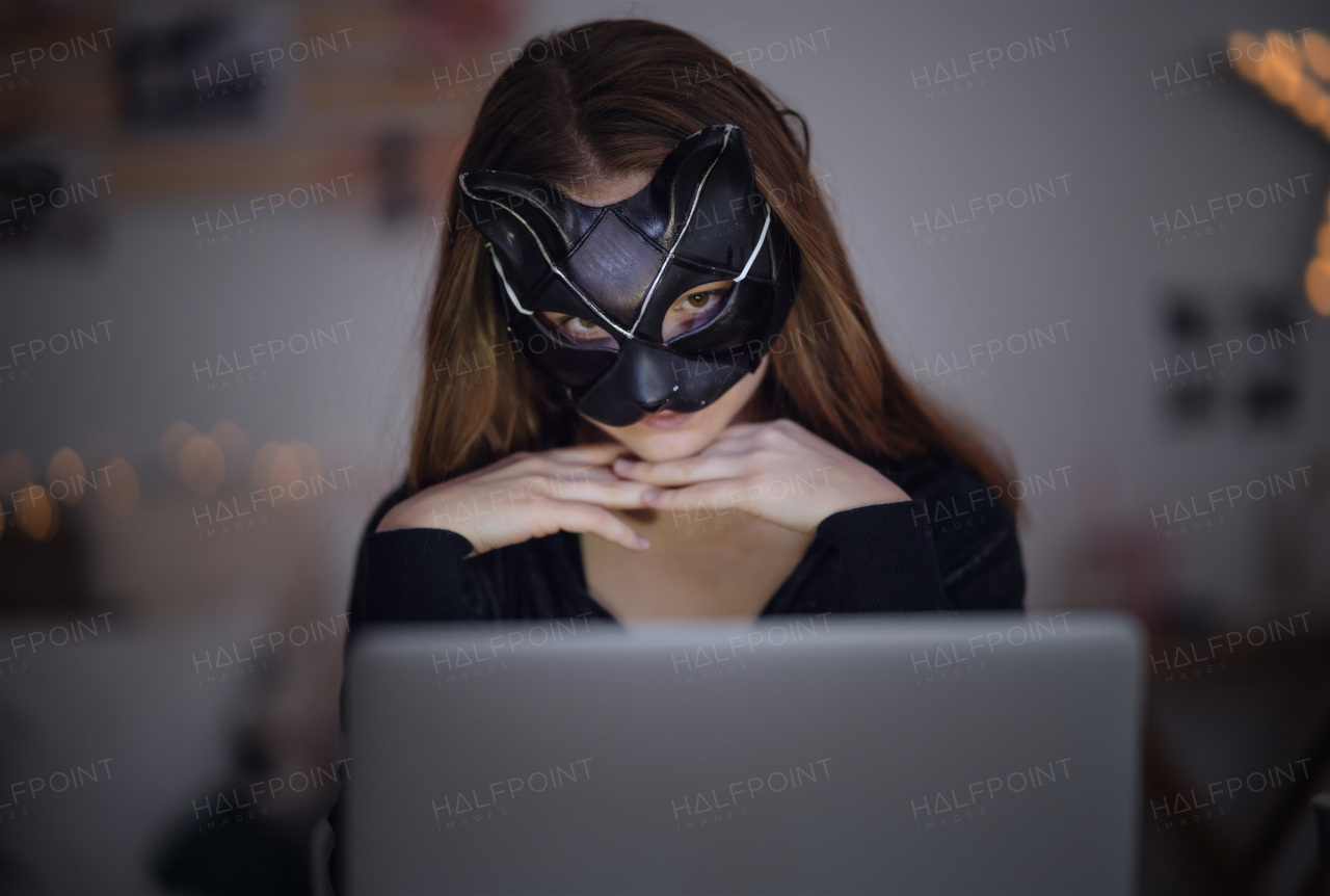 Front view of young girl with cat mask and laptop sitting, online dating and abuse concept.