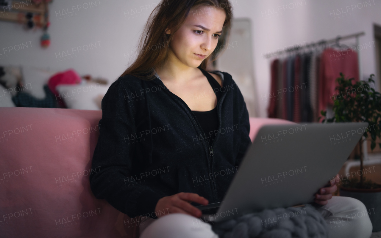 Worried young girl with laptop sitting indoors on floor, online dating and internet abuse concept.