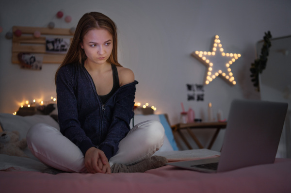 Worried young girl with laptop sitting indoors on floor, online dating and internet abuse concept.