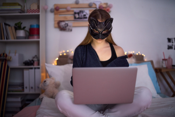 Front view of young girl with cat mask and laptop indoors, online dating and abuse concept.