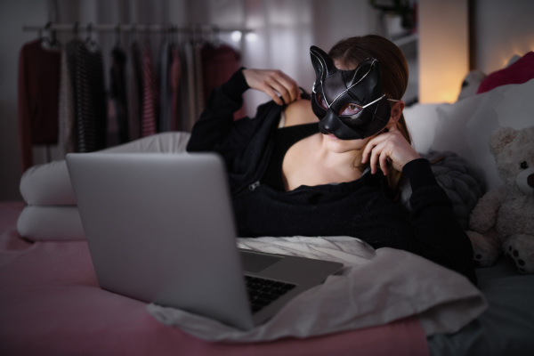 Front view of young girl with cat mask and laptop indoors, online dating and abuse concept.