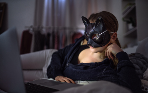 Front view of young girl with cat mask and laptop indoors, online dating and abuse concept.