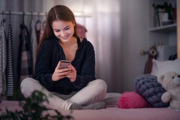 Front view of happy young girl using smartphone on bed, online dating concept.