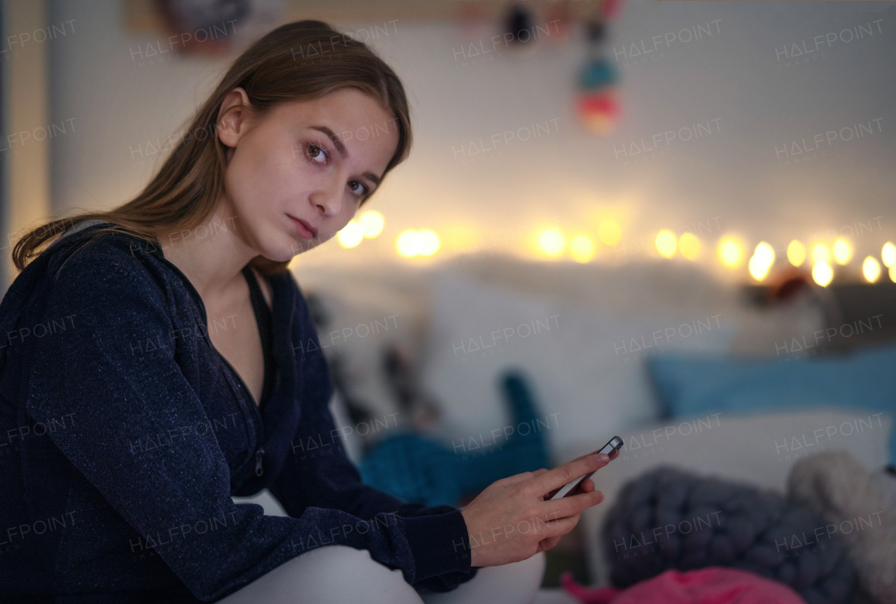 A sad young girl using smartphone on bed, online dating concept.