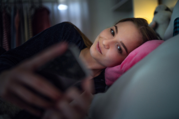 Happy young girl smiling and taking selfie with smartphone on bed, online dating concept.