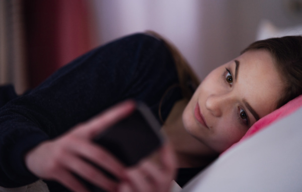 A young girl using smartphone on bed, online dating concept.