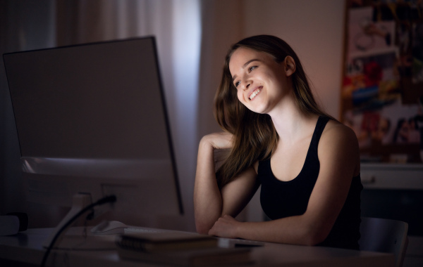 Beautiful happy young girl with computer at night smiling, online dating concept.