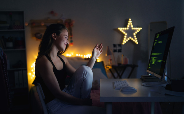 Side view of young girl with headphones and computer sitting indoors, online chatting concept.