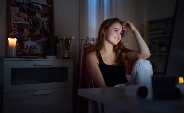 Beautiful happy young girl with computer at night smiling, online dating concept.