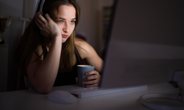 Bored young girl with computer and headphones sitting indoors, internet abuse concept.