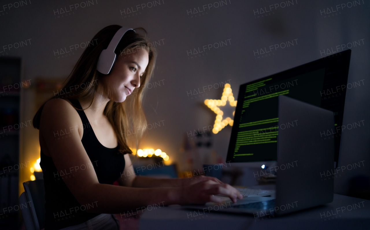 Side view of young girl with headphones and computer sitting indoors, online chatting concept.