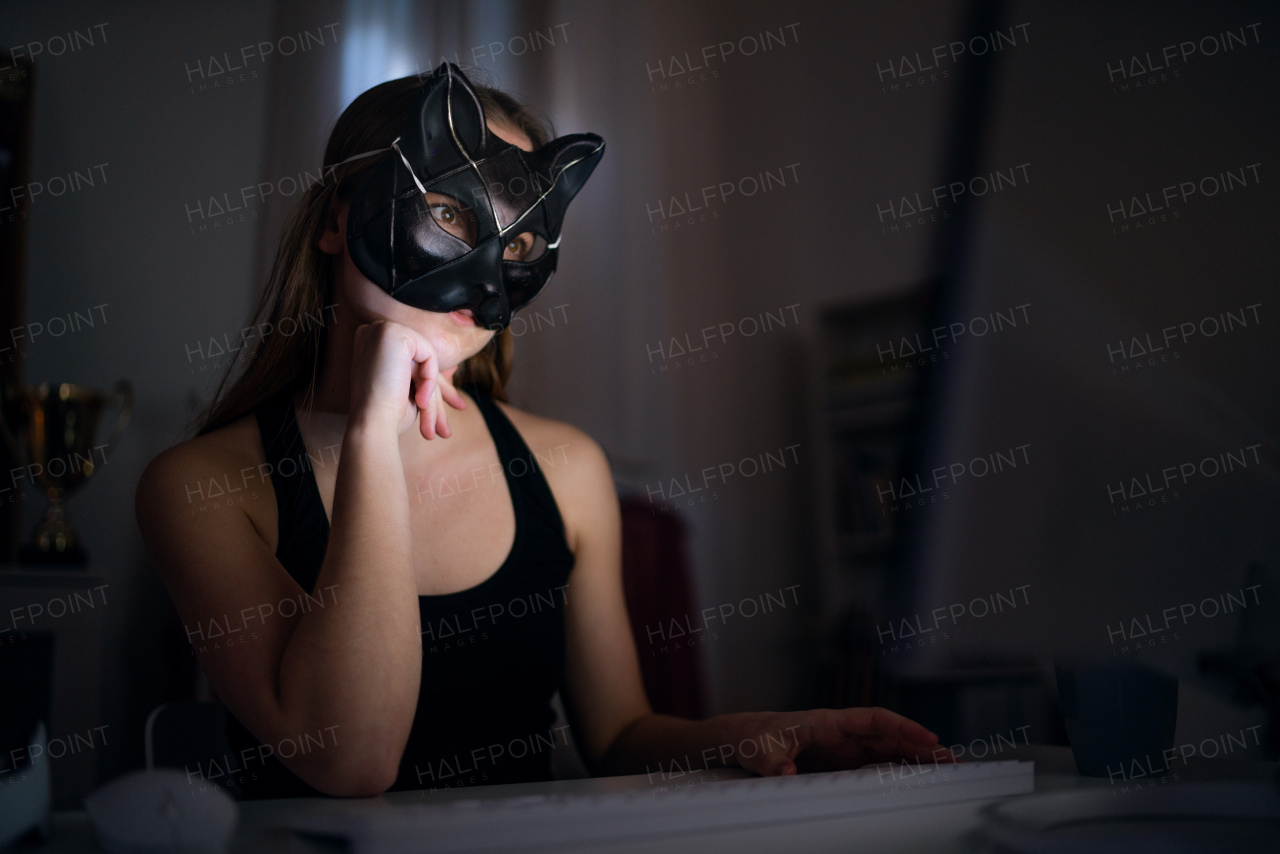 A young girl with cat mask and laptop sitting, online dating and abuse concept.