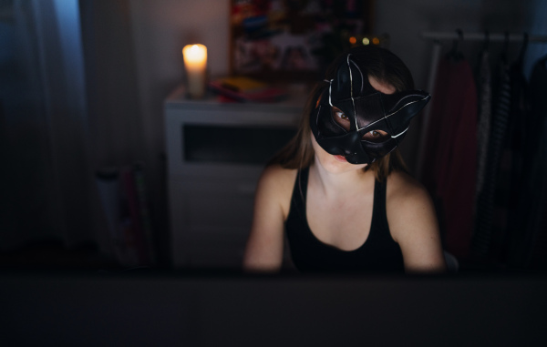 A young girl with cat mask and laptop sitting, online dating and abuse concept.