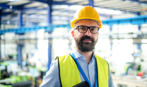 Front view of technician or engineer with hard hat standing in industrial factory, looking at camera.