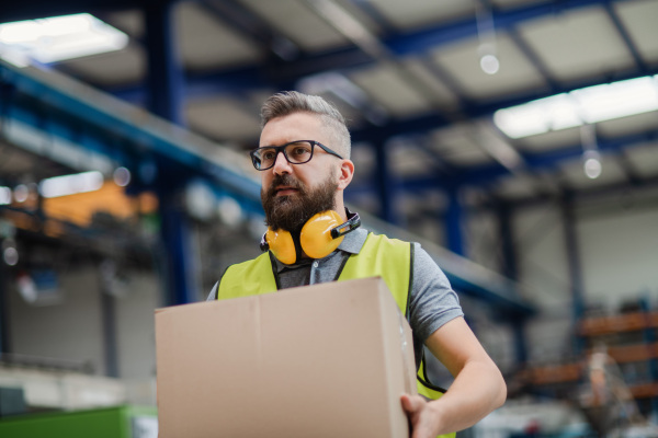 Portrait of man worker working in industrial factory or warehouse, carrying box.