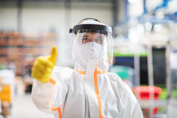 Front view of worker with protective mask and suit in industrial factory, thumb up hand gesture.