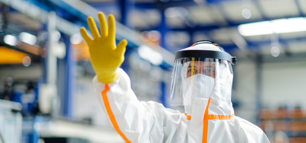 Front view of worker with protective mask and suit in industrial factory, greeting hand gesture.