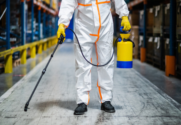 Front view portrait of man worker with protective mask and suit disinfecting industrial factory with spray gun.