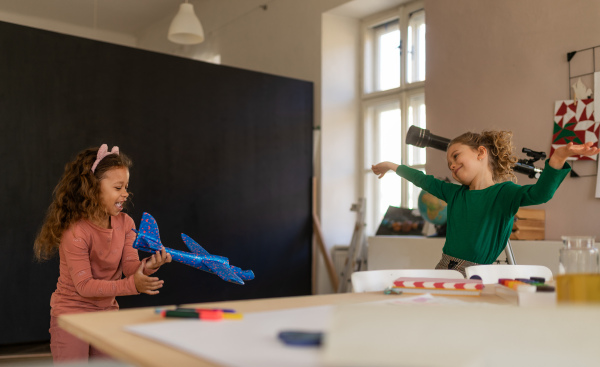 A happy little girl with her friend having fun together at class indoors at school