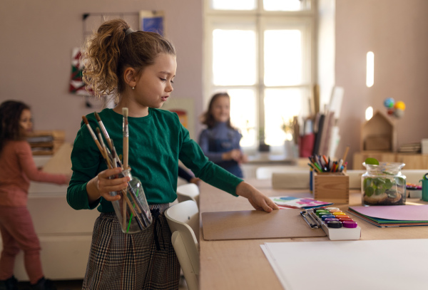 A happy little girl with her friends preparing for art and craft class indoors at school