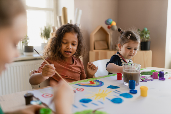 Happy little girls painting a picture during creative art and craft class at school.