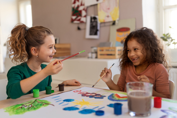 Happy little girls painting a picture during creative art and craft class at school.