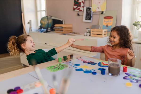 Happy little girls painting a picture during creative art and craft class at school.