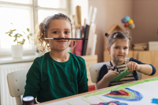 A happy little girl with her friends preparing for art class indoors at school