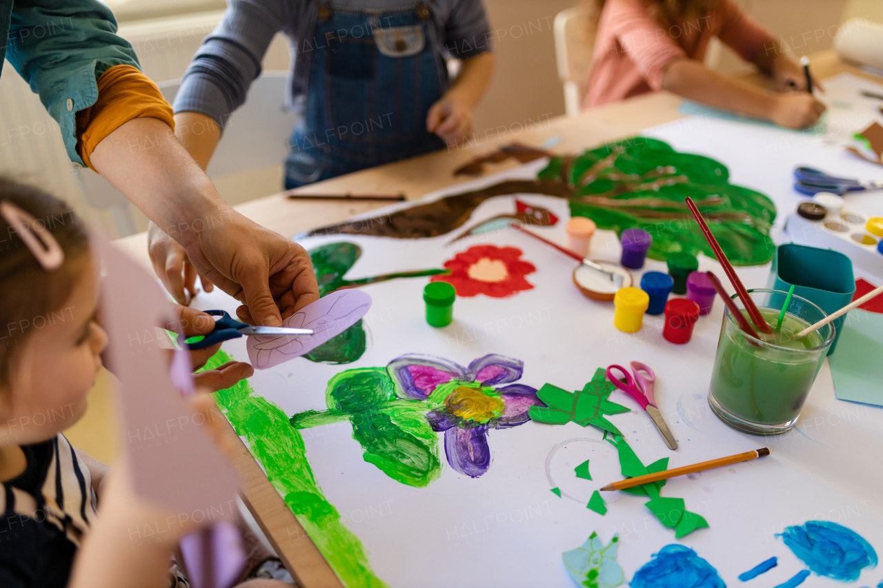 Cloe-up of little kids working on project with teacher during creative art and craft class at school