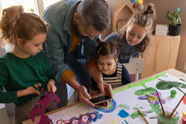 A group of little kids working on project with teacher during creative art and craft class indoors at school.