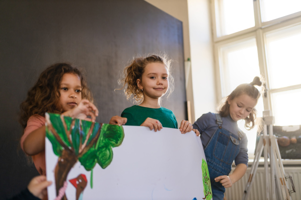 Group of happy little girls holding a picture they painted during creative art and craft class at school