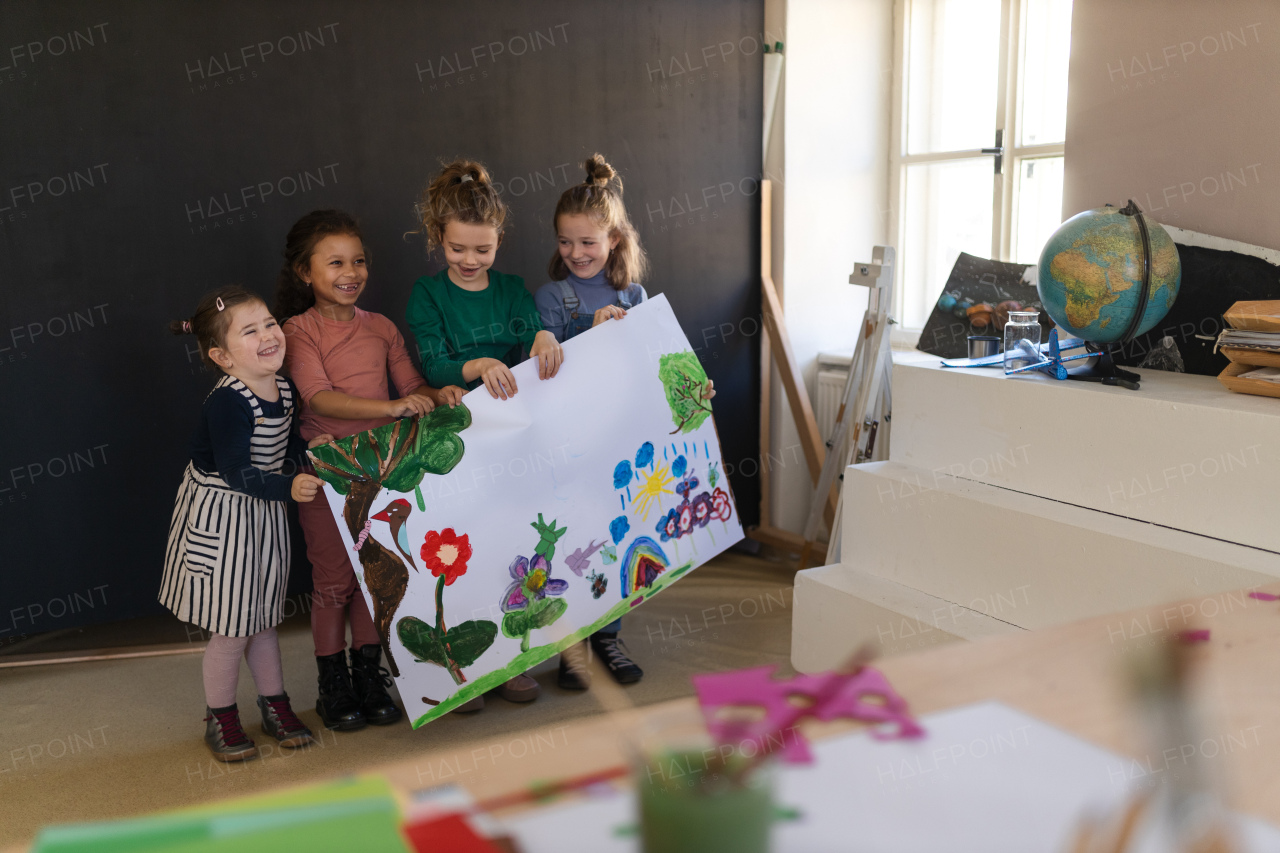 Group of happy little girls holding a picture they painted during creative art and craft class at school