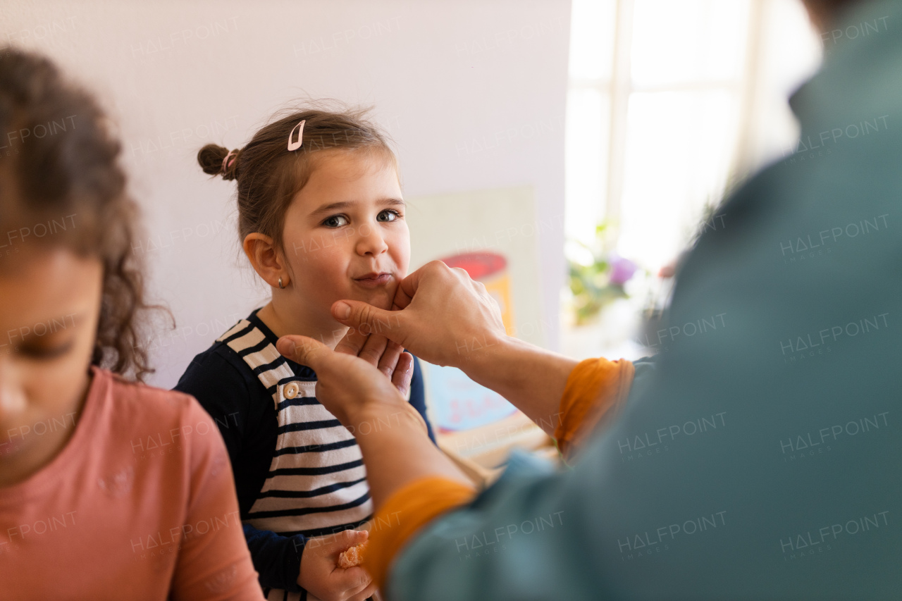 An unrecognizalbe father is cleaning mouth of little daughter when eating fruit at home.