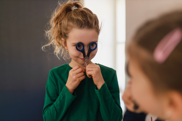 A happy little girl with her friend preparing for art class indoors at school