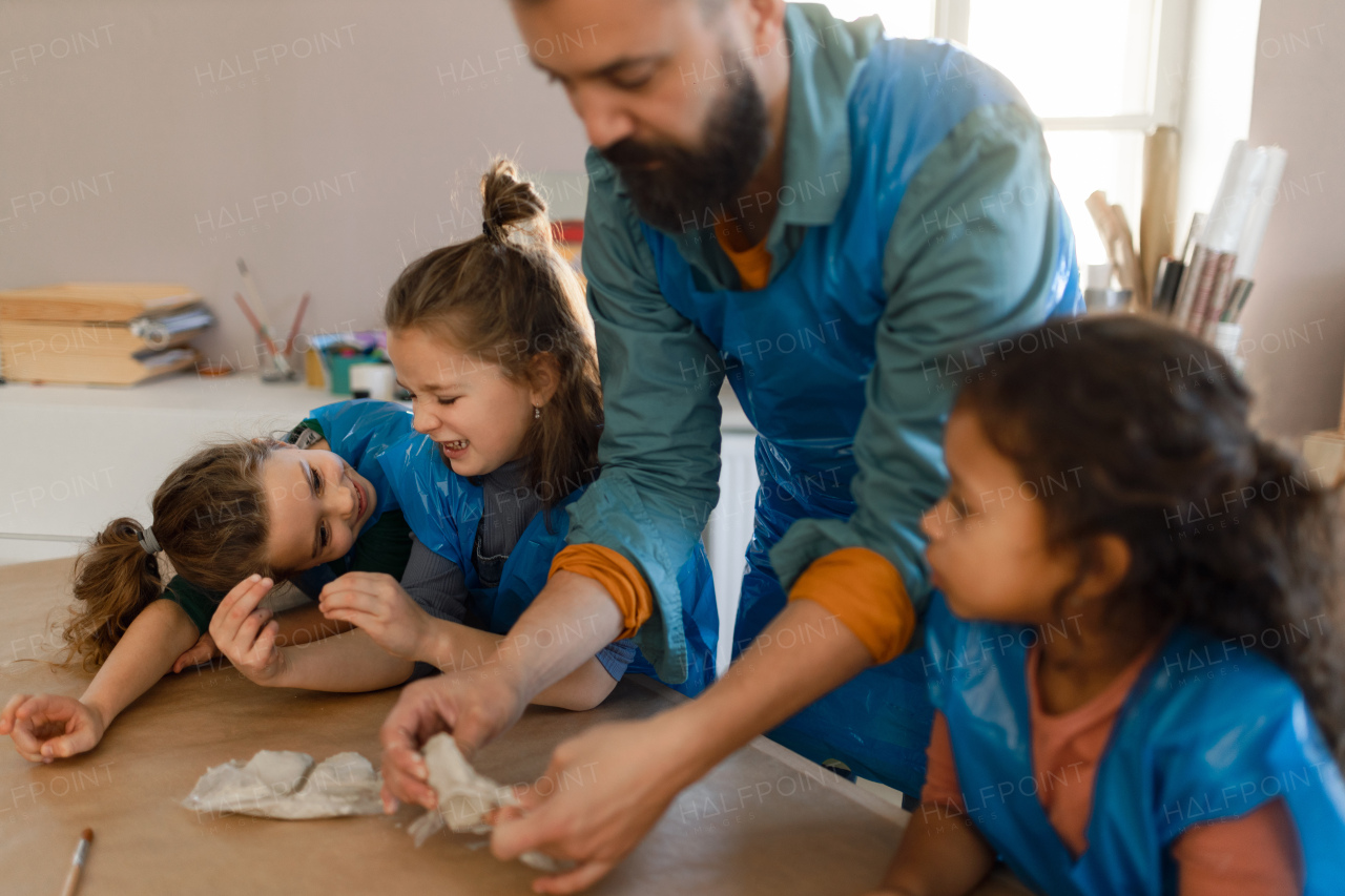 A group of little kids with teacher working with pottery clay during creative art and craft class at school.