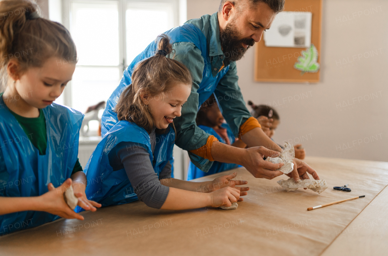 A group of little kids with teacher working with pottery clay during creative art and craft class at school.