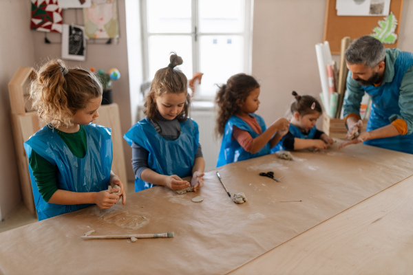 A group of little kids with teacher working with pottery clay during creative art and craft class at school.