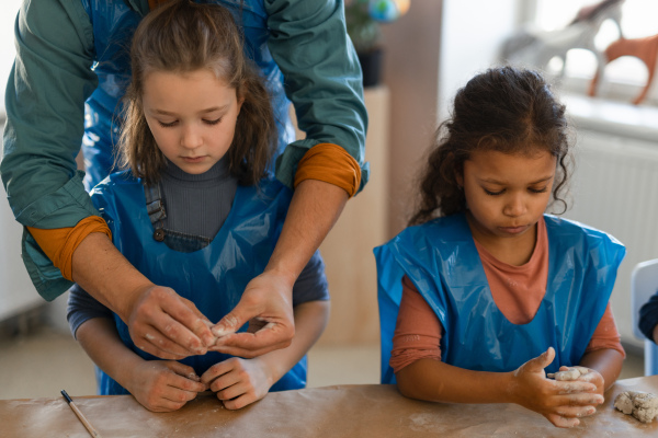 Little kids with a teacher working with pottery clay during creative art and craft class at school.