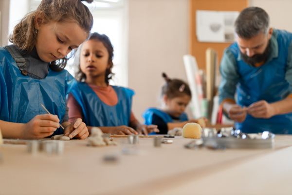 A group of little kids with teacher working with pottery clay during creative art and craft class at school.