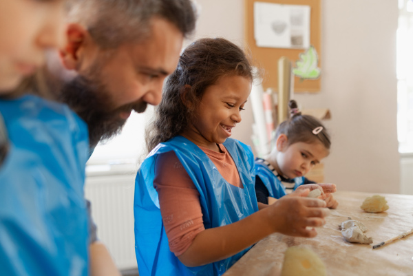 A group of little kids with teacher working with pottery clay during creative art and craft class at school.