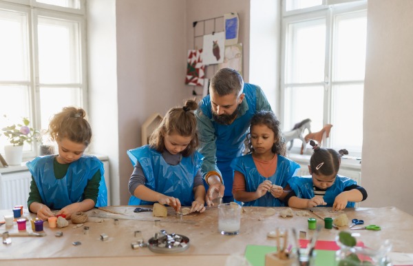 A group of little kids with teacher working with pottery clay during creative art and craft class at school.