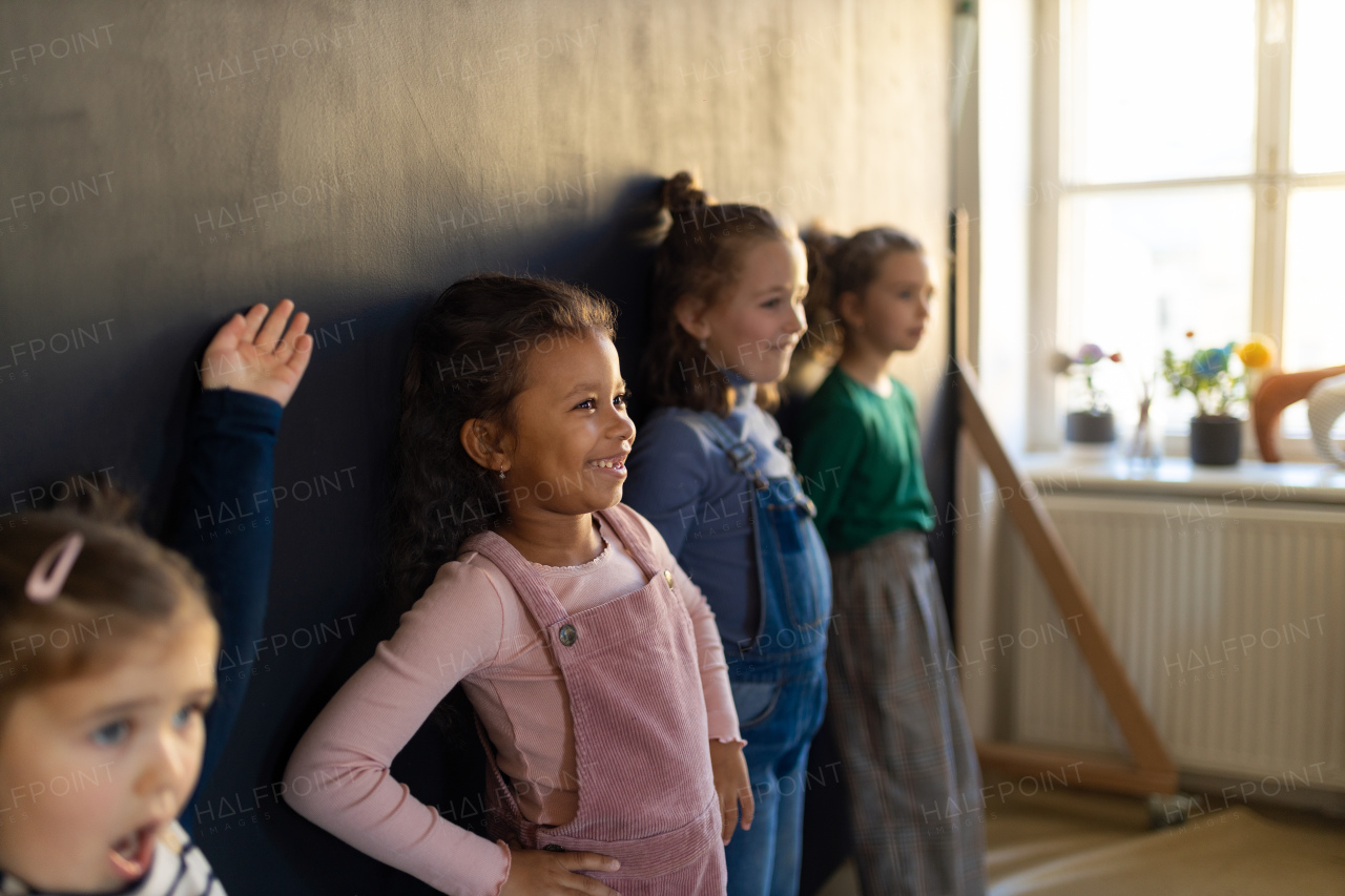 A group of little girls posing in front of blackboard wall paintings indoors in playroom.