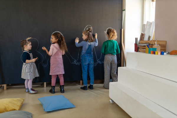 A group of little girls posing in front of blackboard wall paintings indoors in playroom.