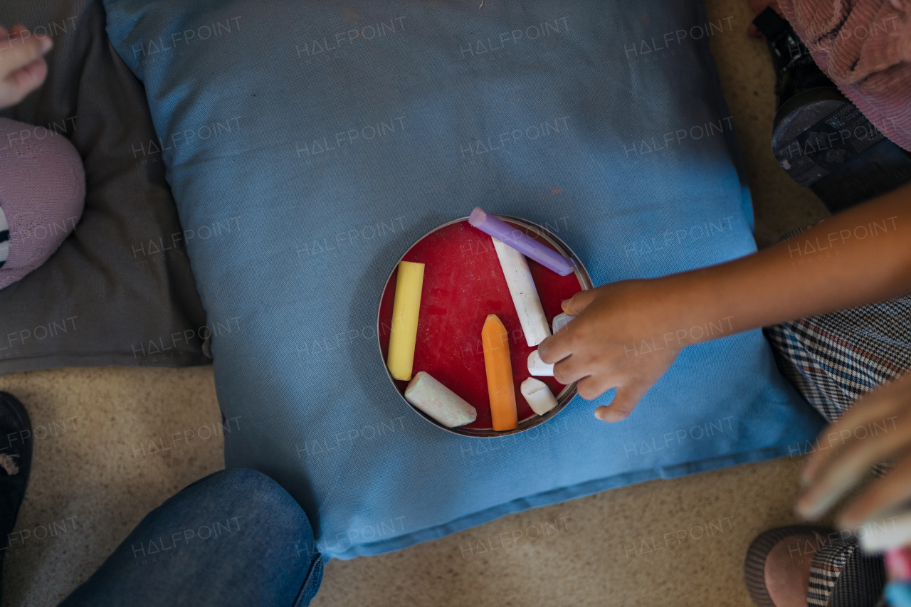 A top view of cildrens hands taking chalks from box indoors in playroom.