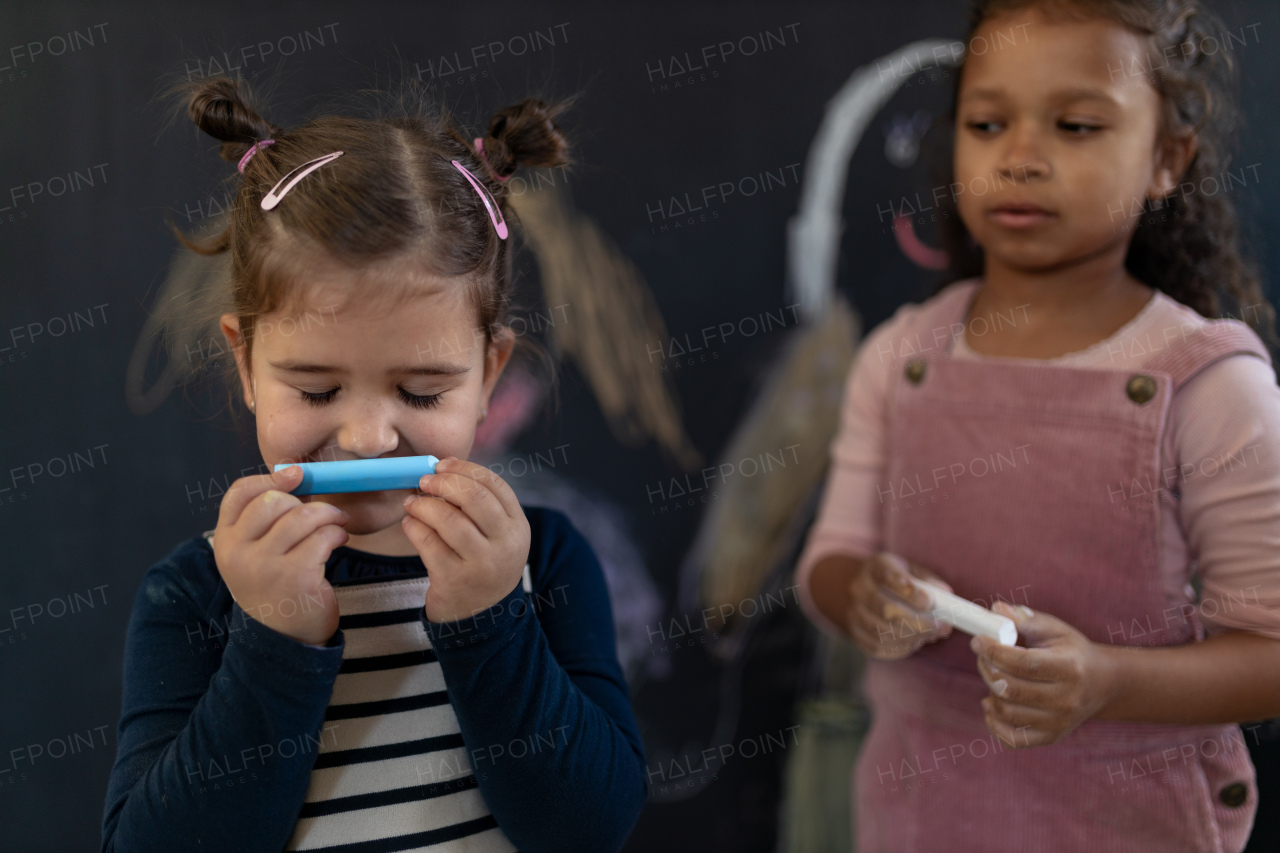 A group of little girls posing in front of blackboard wall paintings indoors in playroom. Smiling and smelling blue chalk.