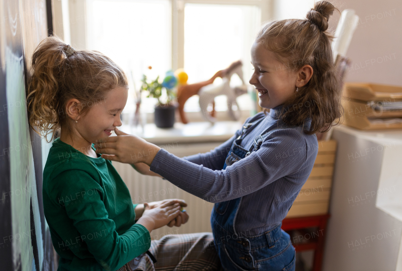 A happy little girl with her friend preparing for art class indoors at school and huving fun