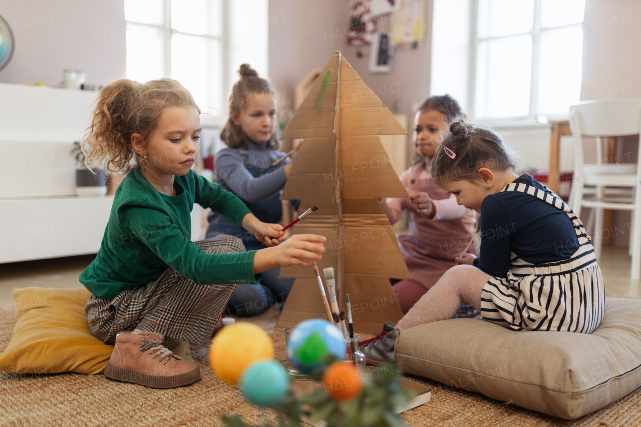 A group of little girls painting cardboard tree at creative art and craft class at school