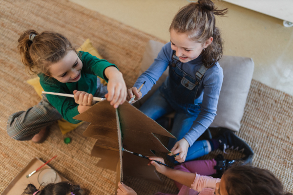 A group of little girls painting cardboard tree at creative art and craft class at school